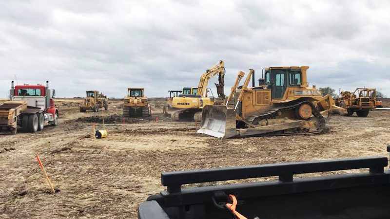 Dozers, excavators and a dump truck working across a flat, cleared tract