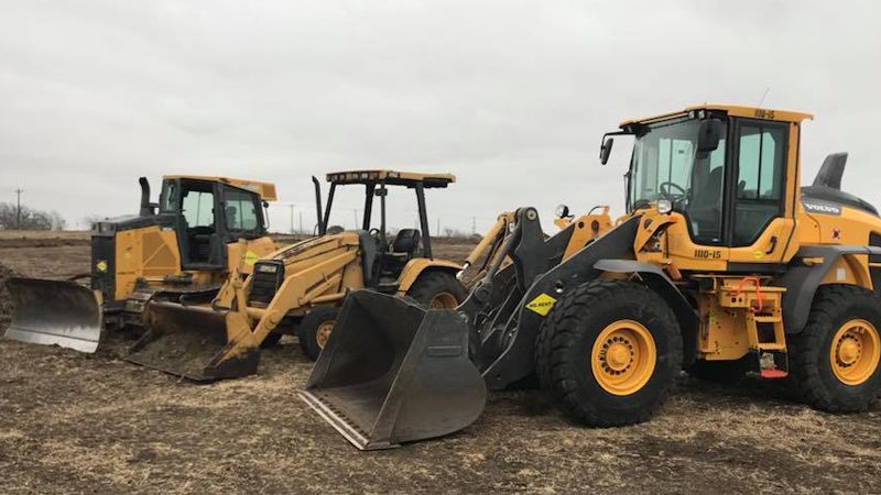 Dozer, backhoe and wheel loader parked on a cleared site under an overcast sky